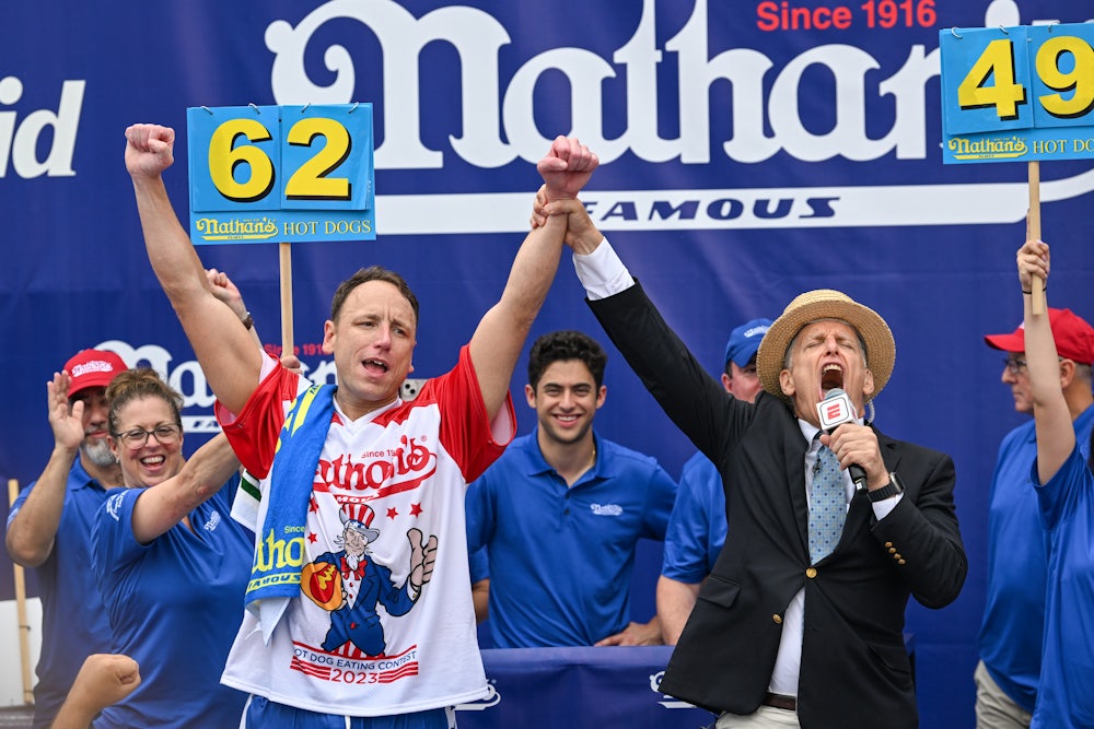 Joey Chestnut raises his hands as an announcer clasps his wrist.