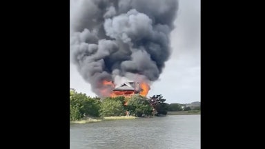 Smoke billows from a burning house by the water.