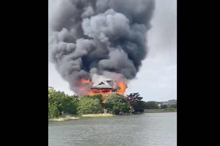 Smoke billows from a burning house by the water.