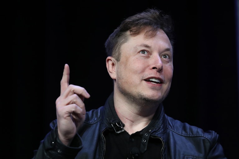 Elon Musk smiles, points a finger upwards 