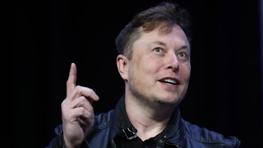 Elon Musk smiles, points a finger upwards