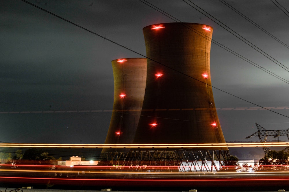 Two nuclear cooling towers rise up from the ground at night with red lights on them and power lines in the foreground.
