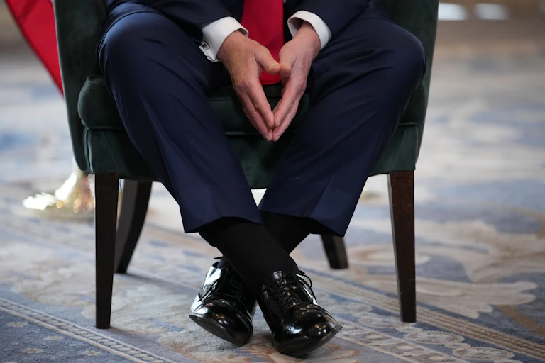 A close-up of Trump's feet in black shoes as he sits on a chair.