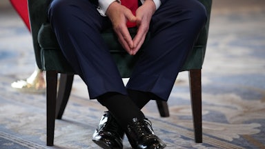 A close-up of Trump's feet in black shoes as he sits on a chair.