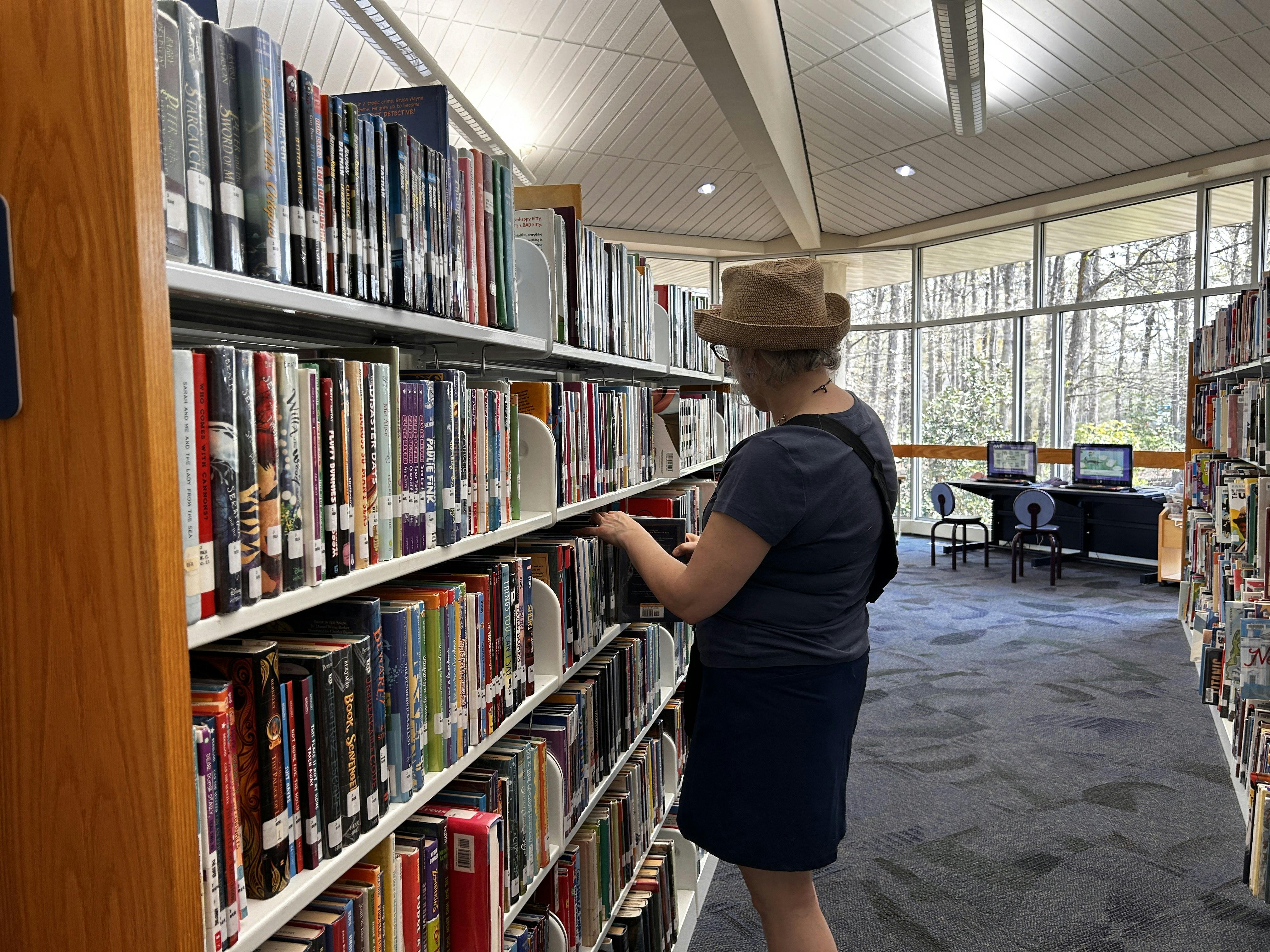 An older woman pulls a book from a bookshelf at the library.