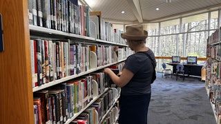 An older woman pulls a book from a bookshelf at the library.