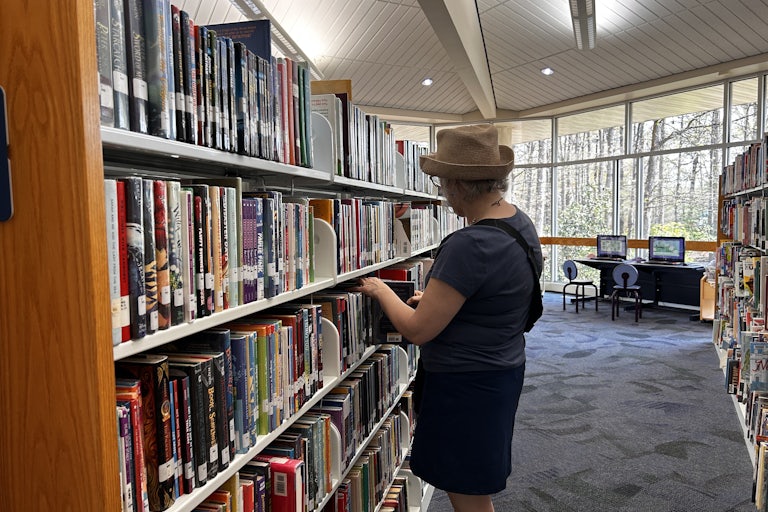 An older woman pulls a book from a bookshelf at the library.