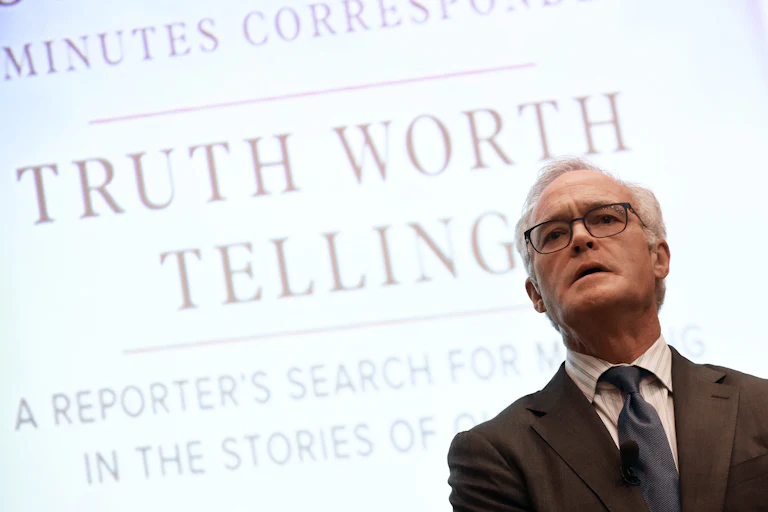 Scott Pelley stands in front of a backdrop that reads "Truth Worth Telling"
