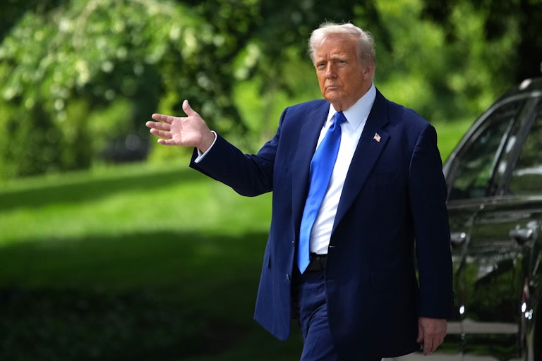 Donald Trump waves as he walks outside. A black car is behind him.