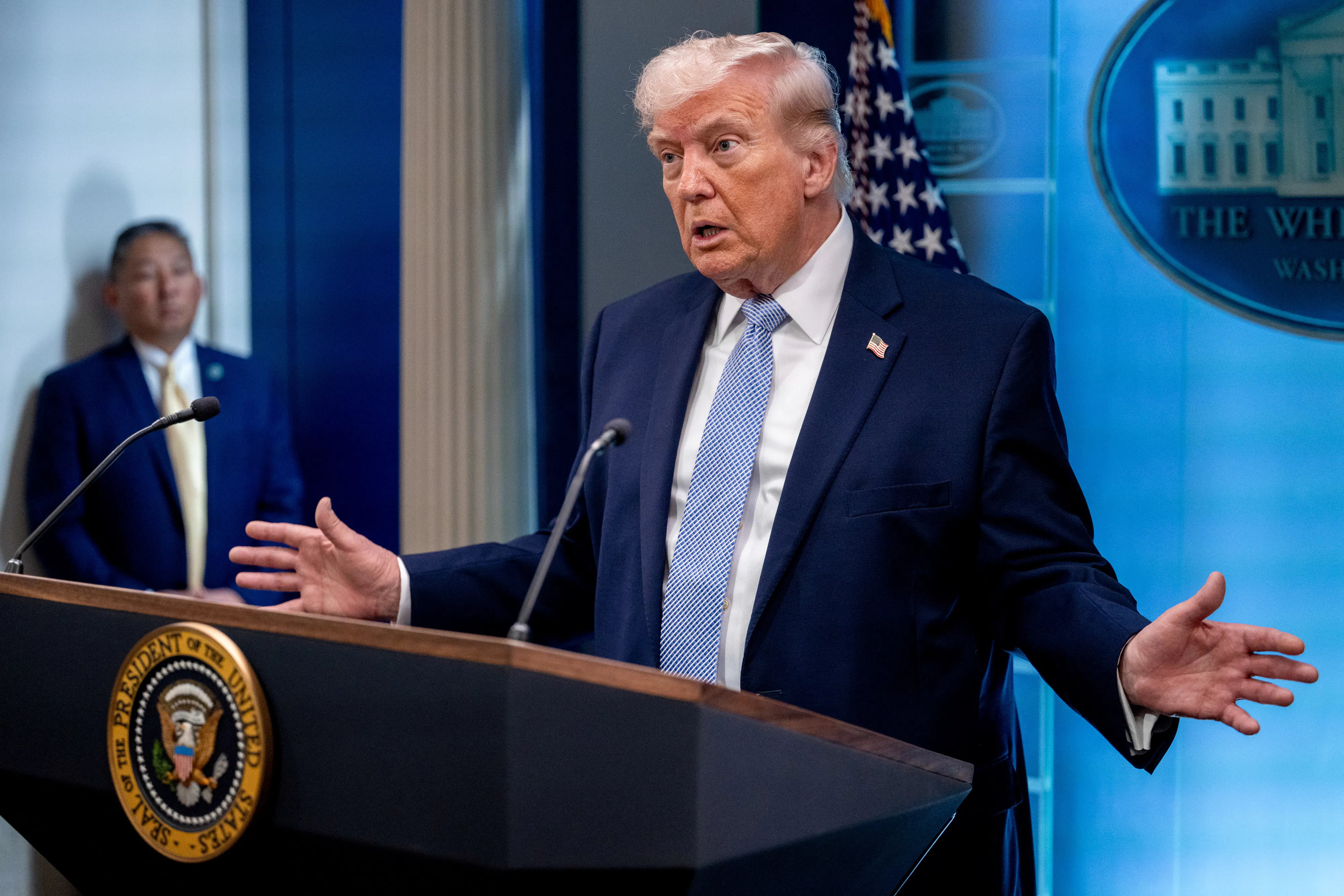 Donald Trump holds his hands out to the side while speaking at a podium during a press conference