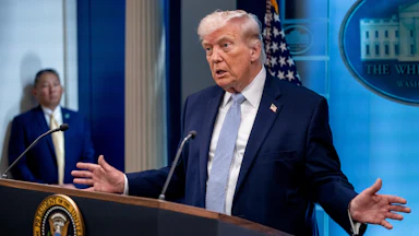 Donald Trump holds his hands out to the side while speaking at a podium during a press conference