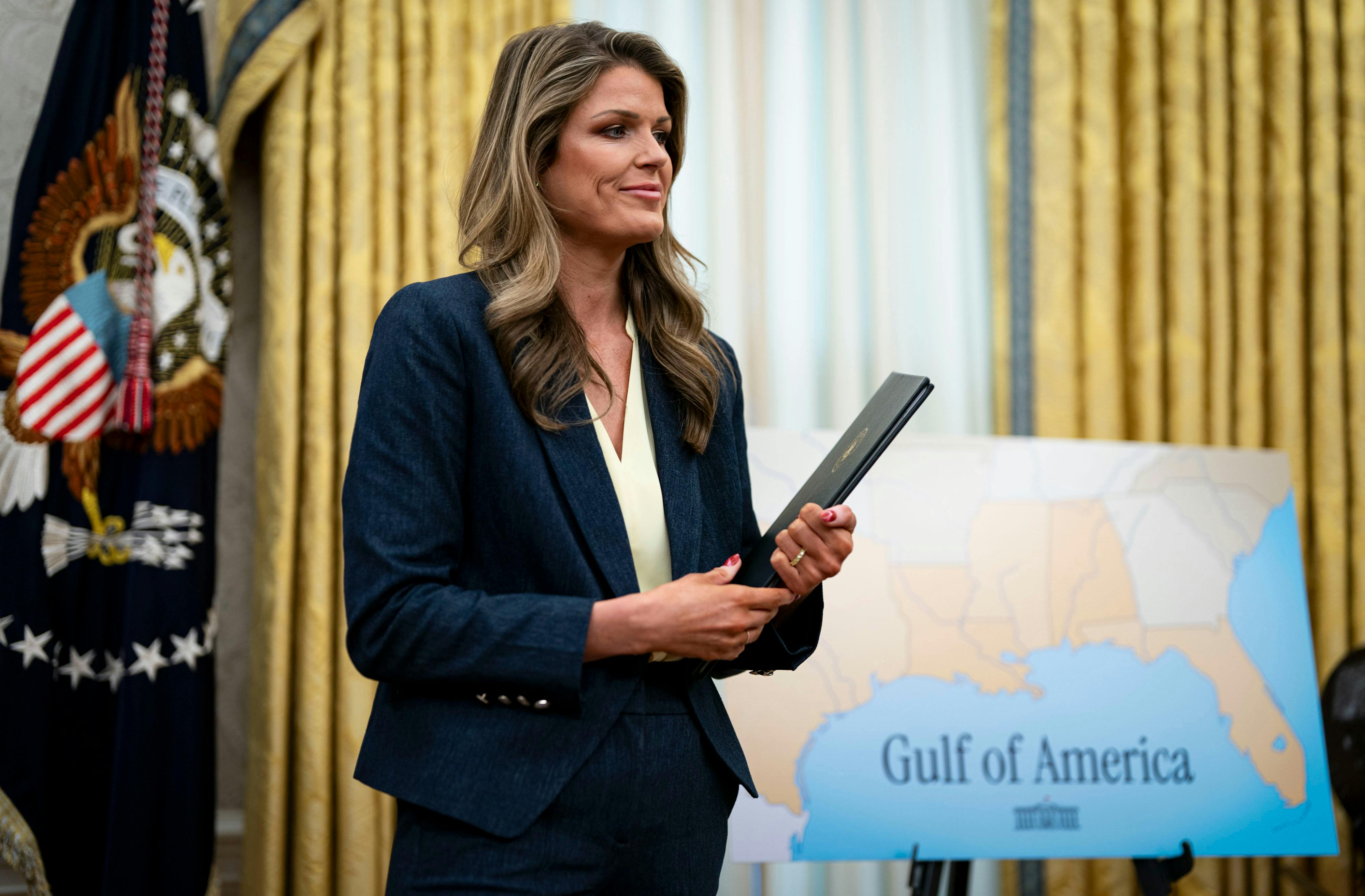 Lindsey Halligan smiles and holds a folder while standing in the Oval Office