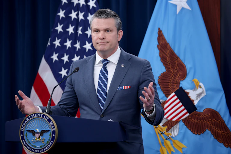 Defense Secretary Pete Hegseth shrugs while standing at a podium