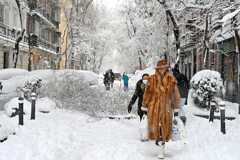 A woman wearing a fur coat walks amid a heavy snowfall in Madrid in January 2021. 