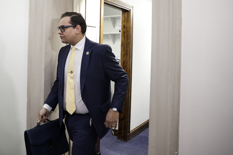 Representative Geroge Santos walks through a doorway with his briefcase in hand