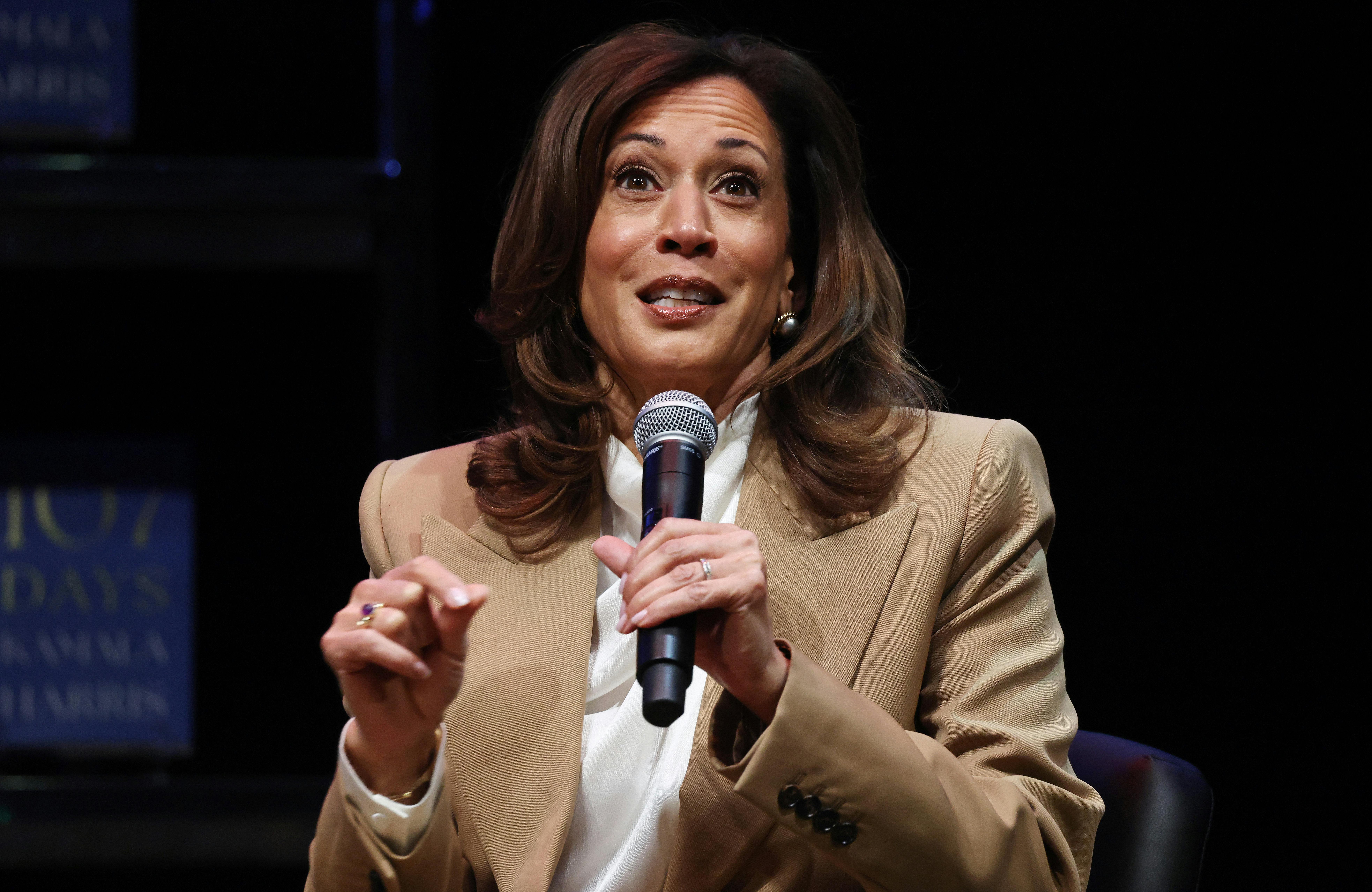 Kamala Harris holds a microphone and gestures while speaking. 