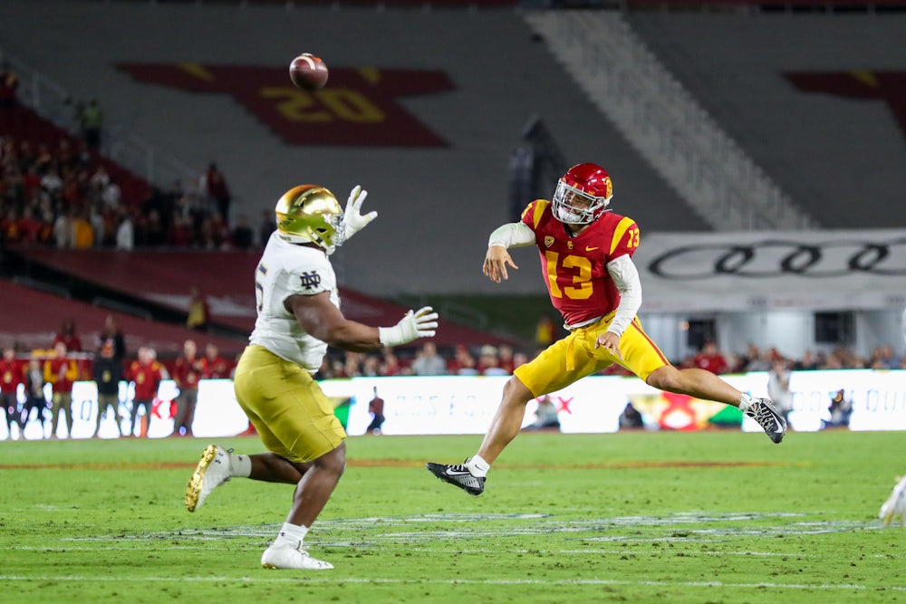 Two football players reach for a ball in the air.