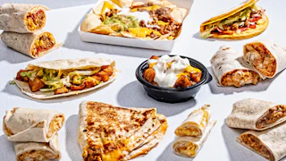 A variety of Taco Bell menu items, from burritos to loaded nachos and other dishes, are seen arrayed on a white background.