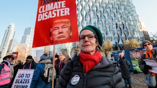 A climate activist wearing a red scarf holds a red placard reading "Trump: Climate Disaster," with other activists in the background.