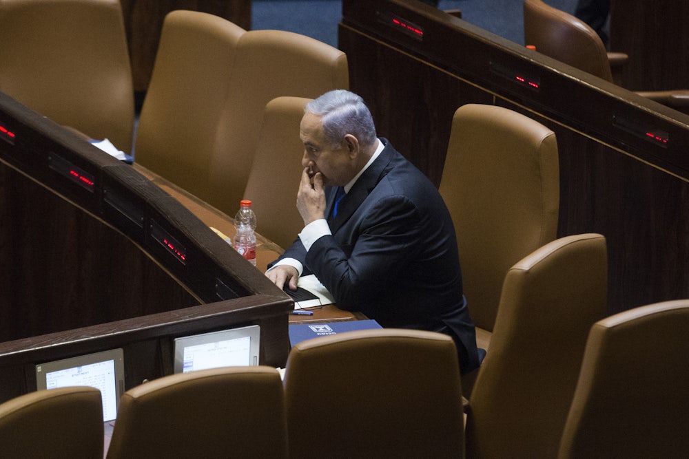 Israeli Prime Minister Benjamin Netanyahu sits alone in an auditorium.