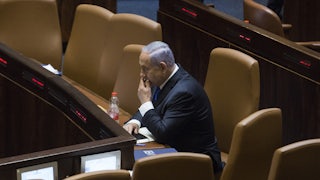 Israeli Prime Minister Benjamin Netanyahu sits alone in an auditorium.