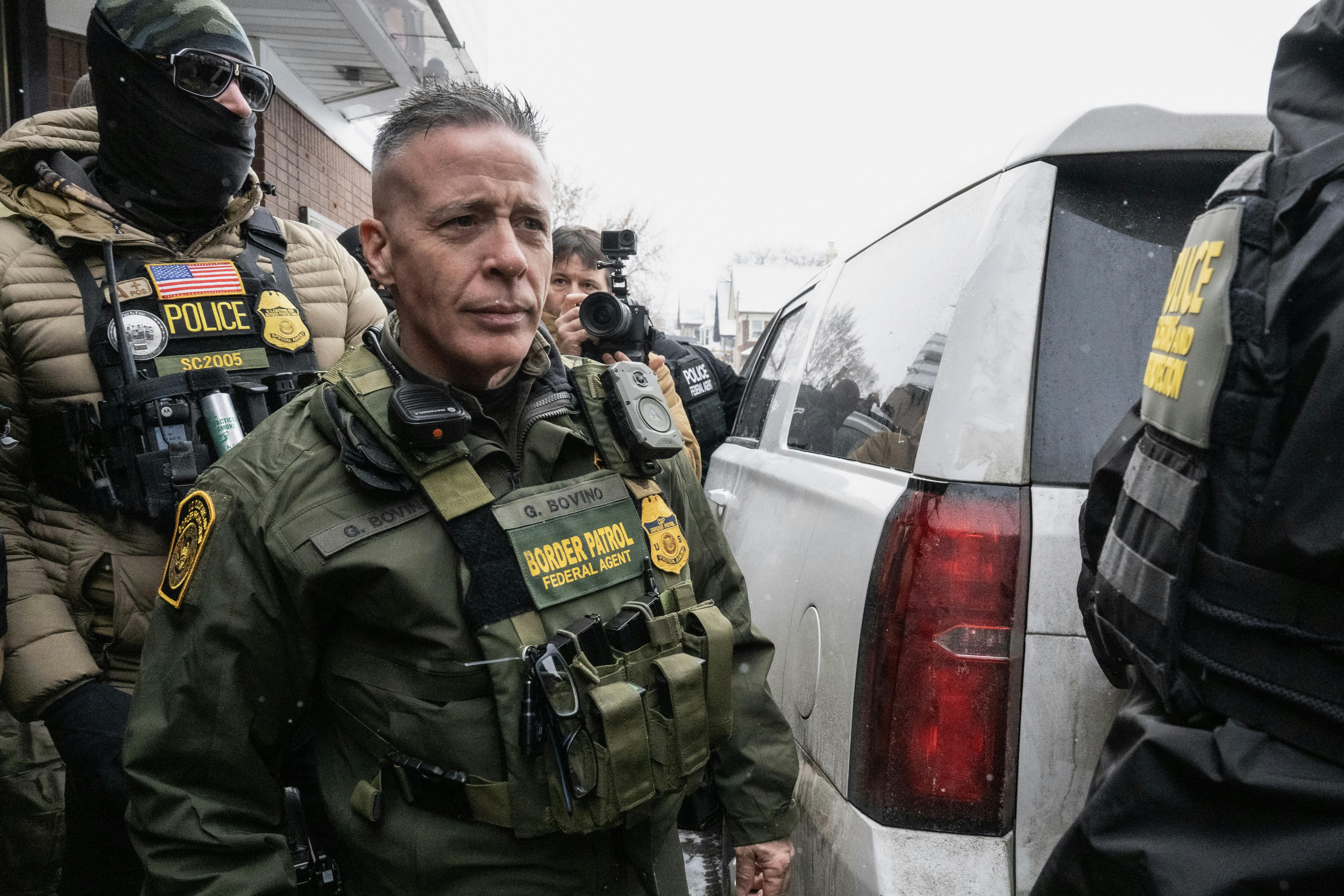 U.S. Border Patrol commander Gregory Bovino walks to his car as masked federal agents surround him.