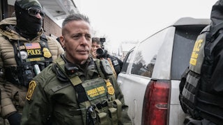 U.S. Border Patrol commander Gregory Bovino walks to his car as masked federal agents surround him.