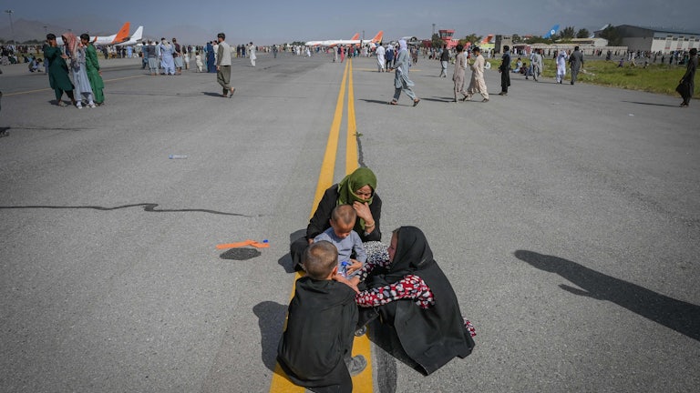 An Afghan woman and three children huddle on the tarmac of the airport in Kabul, Afghanistan.