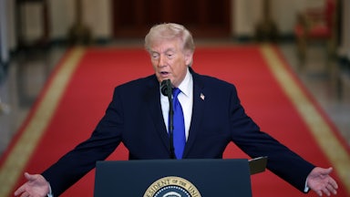 Donald Trump speaks at a presidential podium and stretches out both arms as if in exasperation.