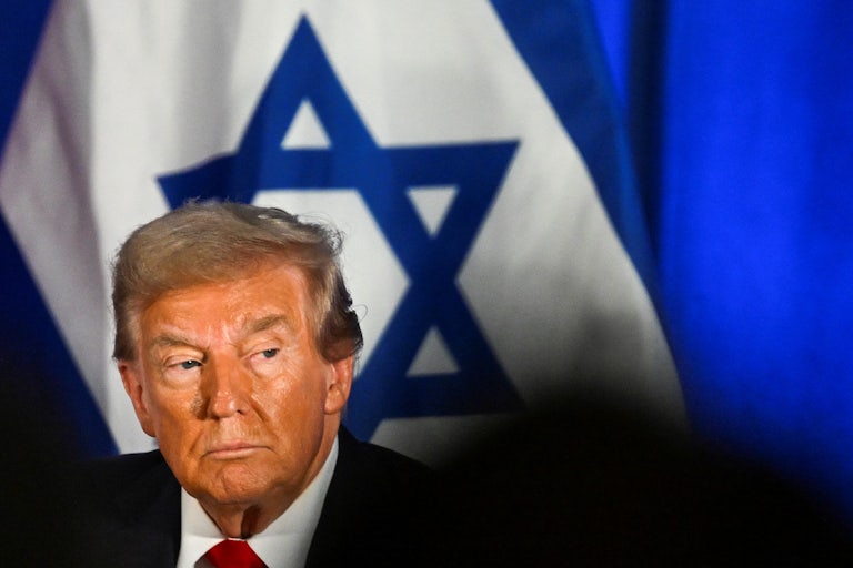 Donald Trump looks to the side while sitting in front of an Israeli flag