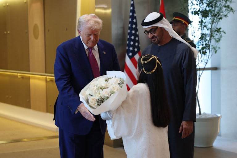 Trump takes a large bouquet of flowers from a girl in traditional attire as Zayed Al Nahyan stands next to him talking to the girl and smiliing.