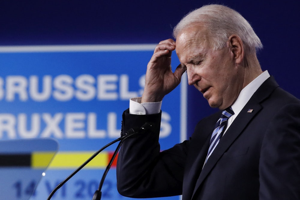 Joe Biden reaches a hand to his head while speaking into a microphone.