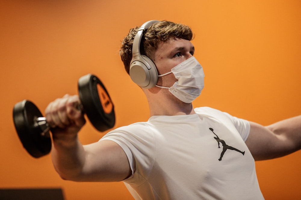 A person lifts weights in a gym while wearing a Covid face mask