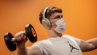 A person lifts weights in a gym while wearing a Covid face mask