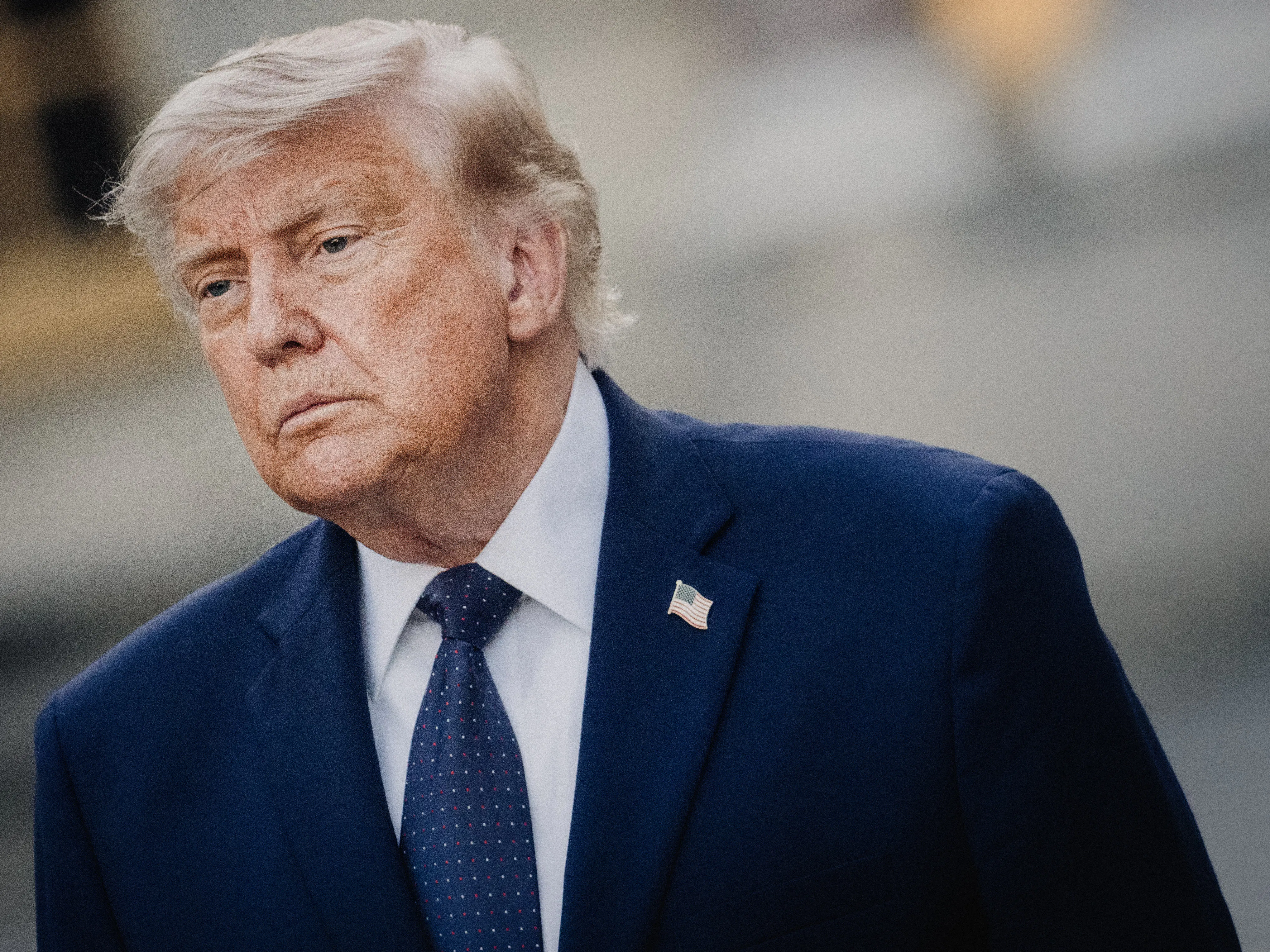 Donald Trump, wearing a blue suit and blue tie, stands at an angle. 