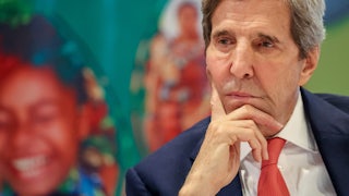 John Kerry sits with his head on his chin, looking contemplative.
