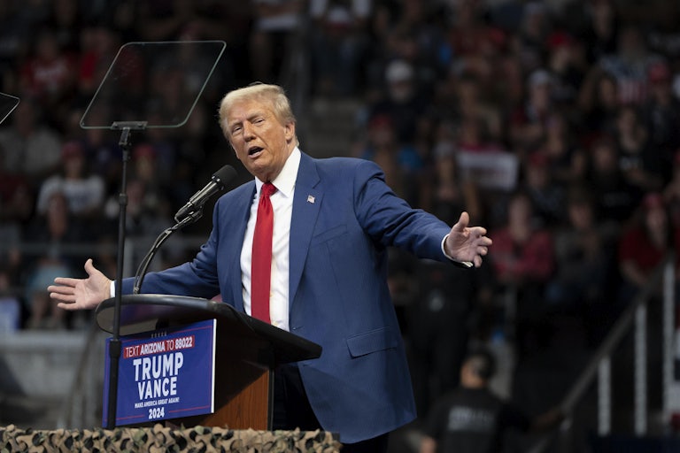 Donald Trump holds his arms out and looks to the side while speaking at a campaign event