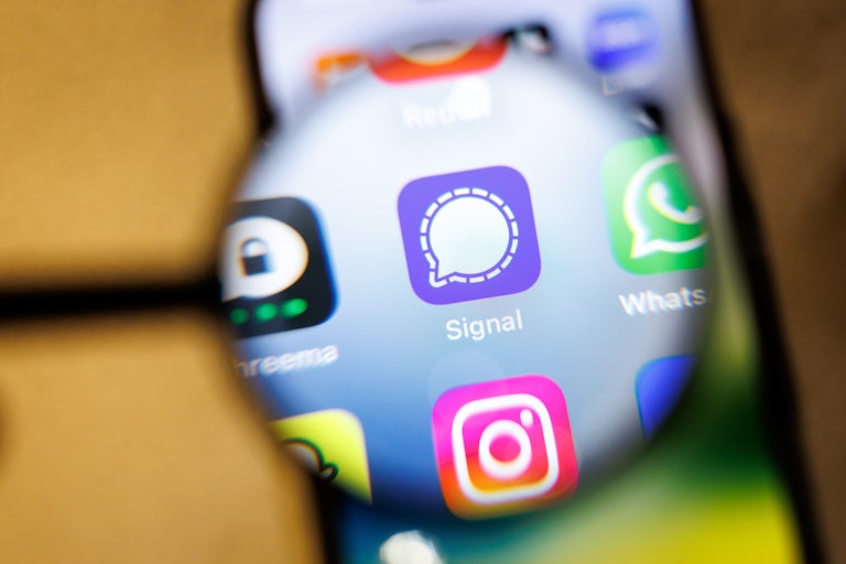 A magnifying glass over the home screen of a smartphone highlights the messaging app Signal.