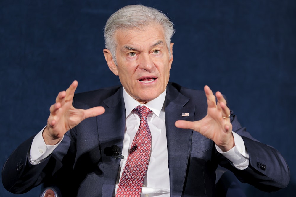 Dr. Oz is seen from the waist up, speaking while seated and raising both hands while talking.