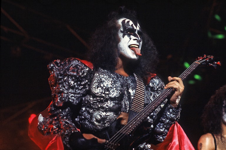 Gene Simmons sticks his tongue out while playing the bass. He is wearing his "demon" make up.