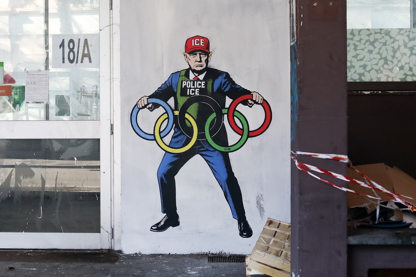 A mural created for the Milano-Cortina Winter Olympics, depicting President Trump wearing an ICE police uniform and a red cap with the ICE logo, while holding the five Olympic rings. 