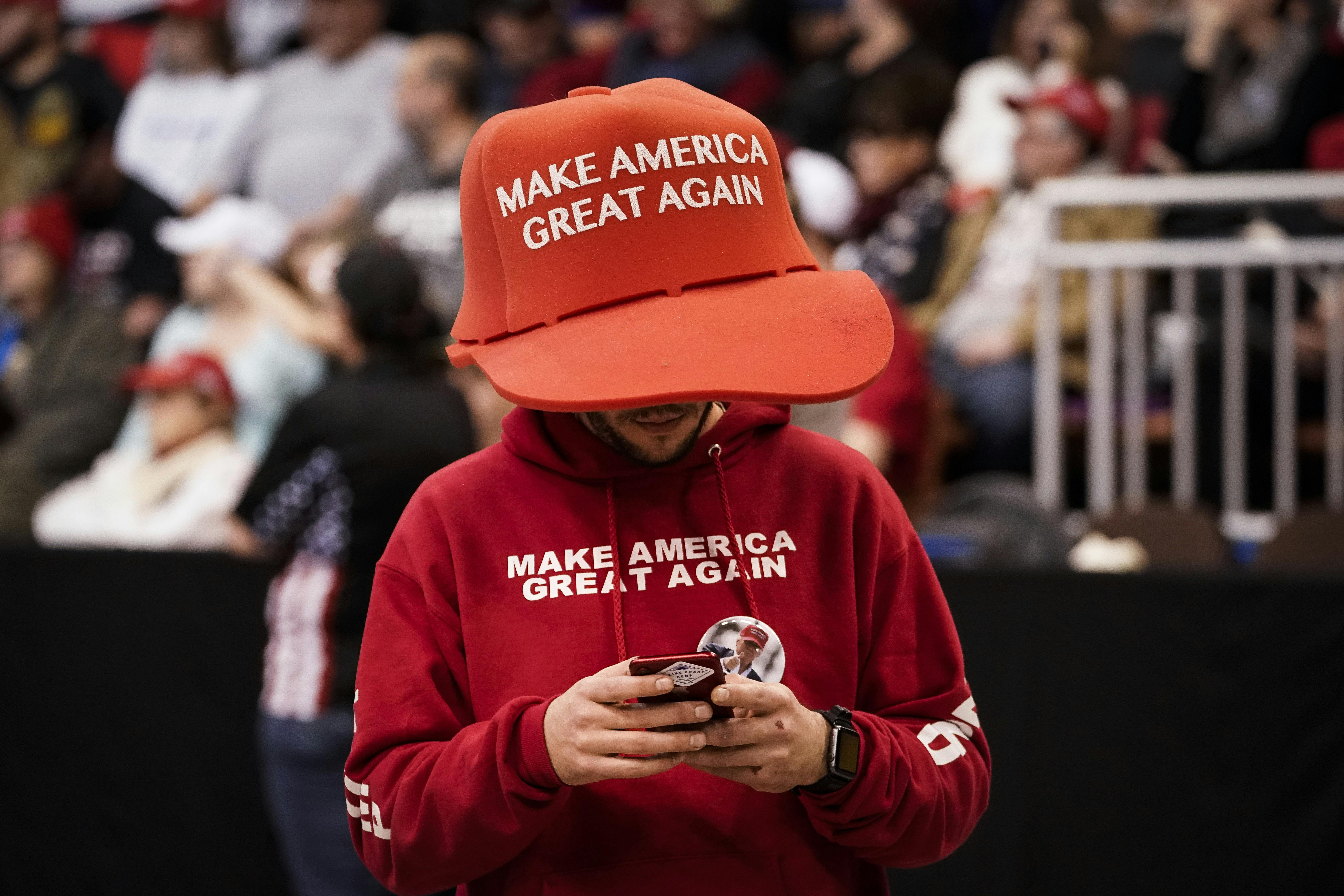 A supporter of Donald Trump wears an oversize "Make America Great Again Hat" as he texts.