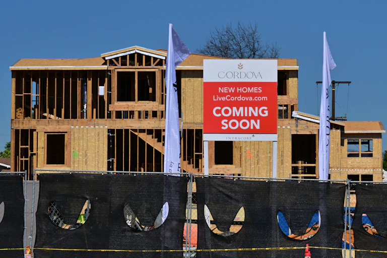 Plywood and wood framing are visible on a home still under construction, with a "Cordova New Homes Coming Soon" sign visible in front of the house frame.