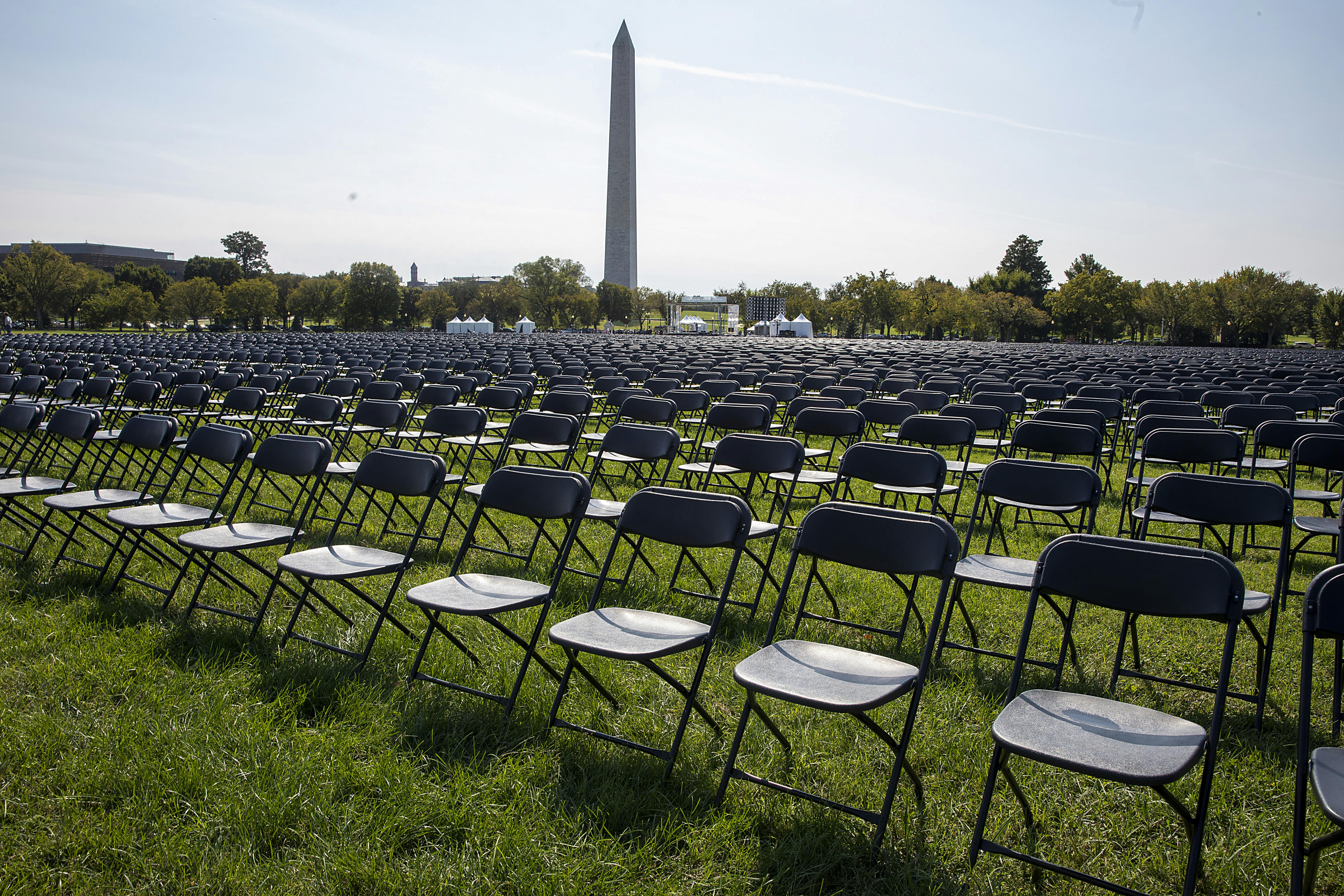 Rows and rows of empty chairs stand on grass, with the Washington Monument in the background.