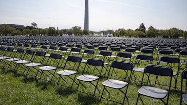 Rows and rows of empty chairs stand on grass, with the Washington Monument in the background.
