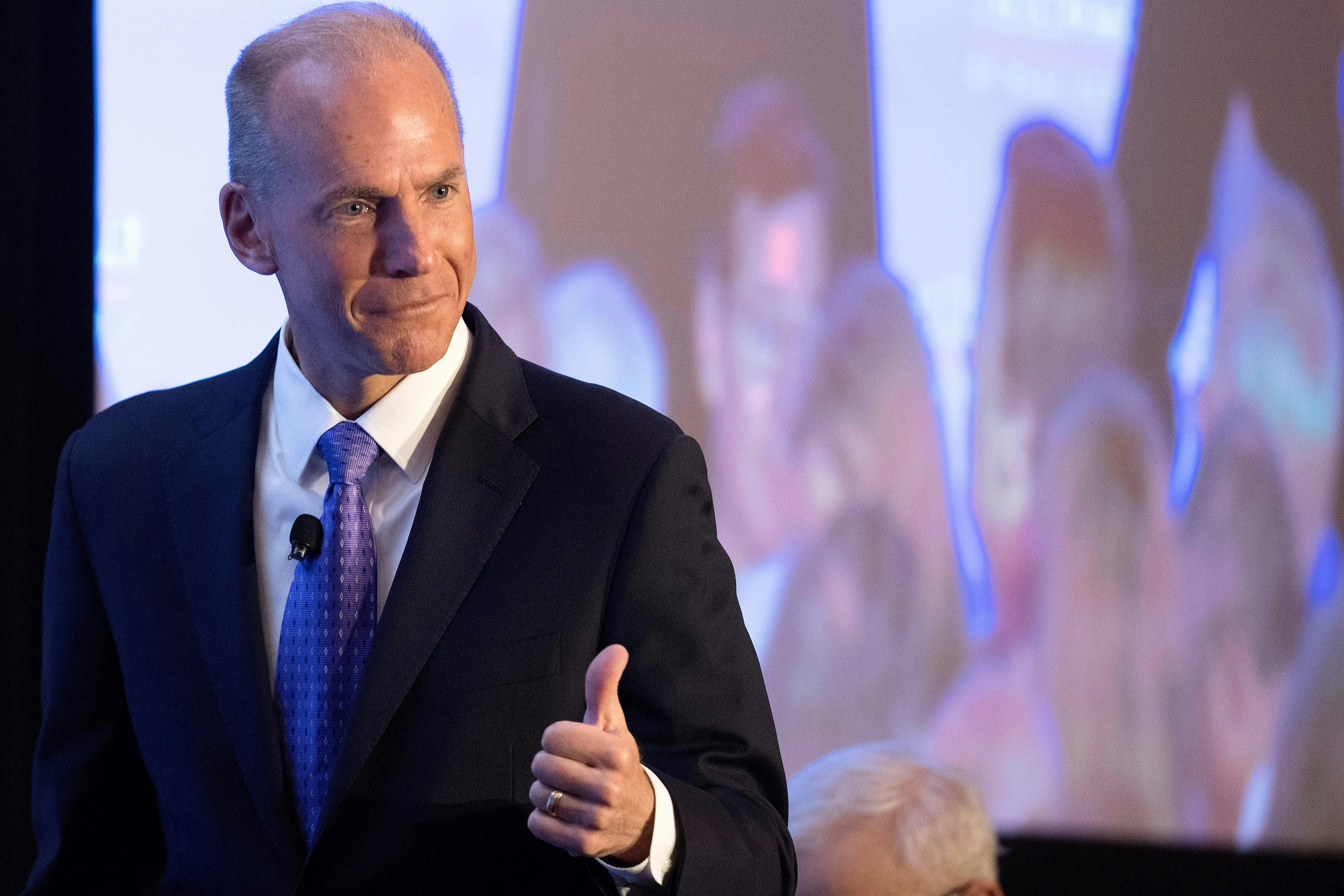 Former Boeing CEO Dennis Muilenburg gives a thumbs up gesture in front of a screen.