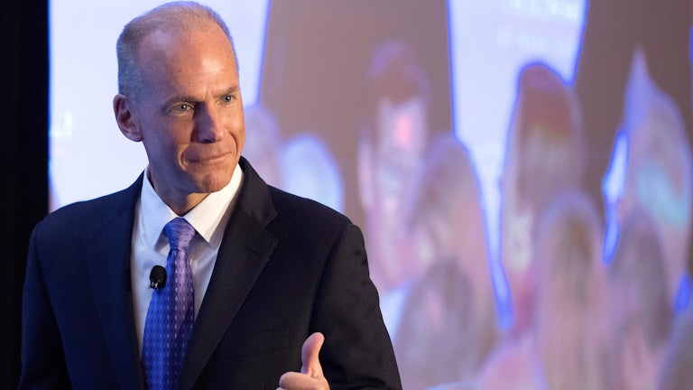 Former Boeing CEO Dennis Muilenburg gives a thumbs up gesture in front of a screen.