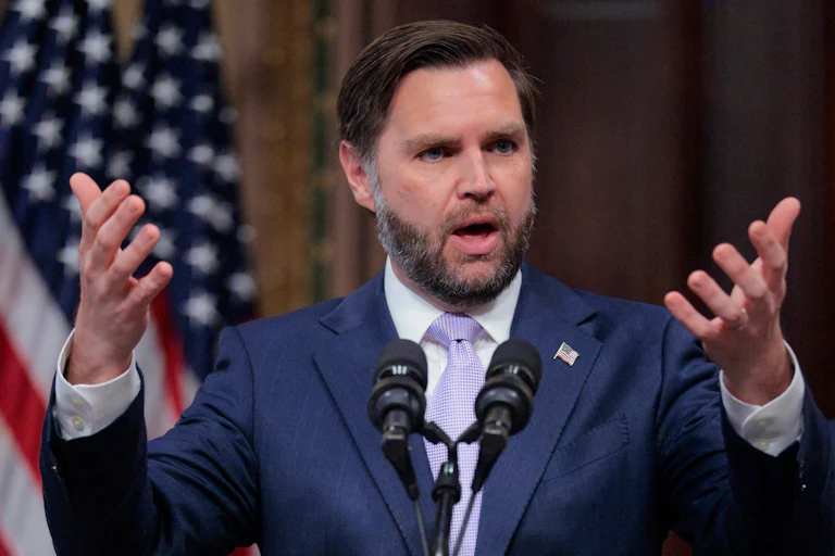 Vice President JD Vance holds out his hands while speaking at a podium