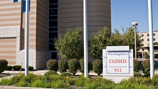 A sign in front of a hospital that reads THIS HOSPITAL IS CLOSED IF THIS IS AN EMERGENCY CALL 911
