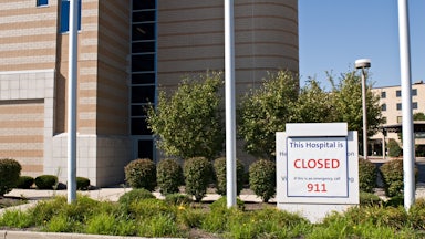 A sign in front of a hospital that reads THIS HOSPITAL IS CLOSED IF THIS IS AN EMERGENCY CALL 911